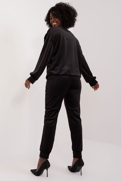Rear view of Italy Moda velour sweatshirt and pants set in black, underlining the sleek silhouette and modern fit. Model looks over her shoulder, showcasing elegance and poise.