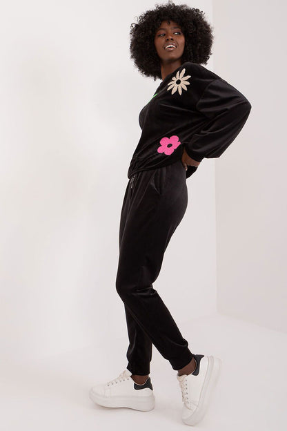 Side view of a model in the luxurious black floral velour set by Italy Moda, showcasing the stylish design and floral details on the sweatshirt, matched with sophisticated black high-waisted pants and fashionable white trainers.