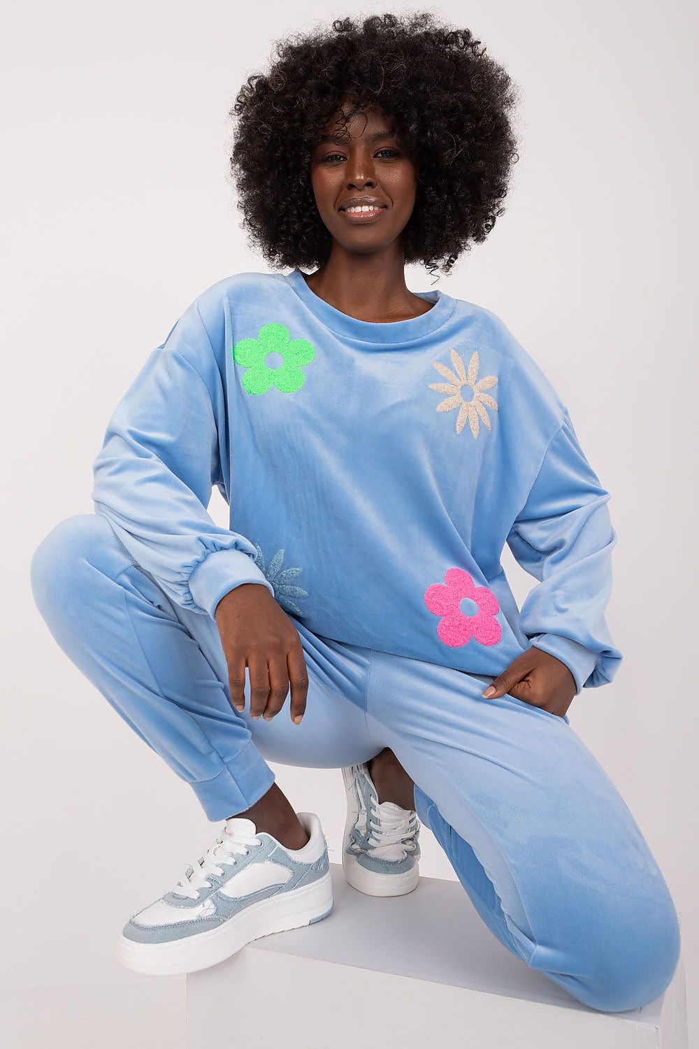Close-up of a model in a blue floral velour set by Italy Moda, highlighting the intricate floral designs on the sweatshirt and pants for a trendy flair.
