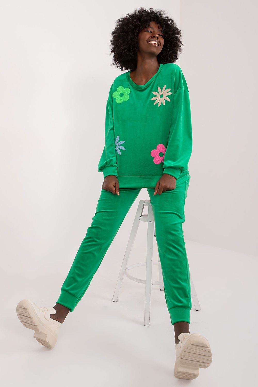 Chic green velour sweatshirt and matching high waisted pants decorated with vibrant flowers, styled on a model, by Italy Moda.