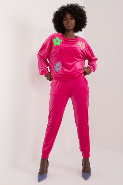 Vibrant pink velour set by Italy Moda, adorned with colourful floral embroidery. Model exudes luxury in this fashionable sweatshirt and high-waisted pant combination, showcasing a chic and comfortable look.
