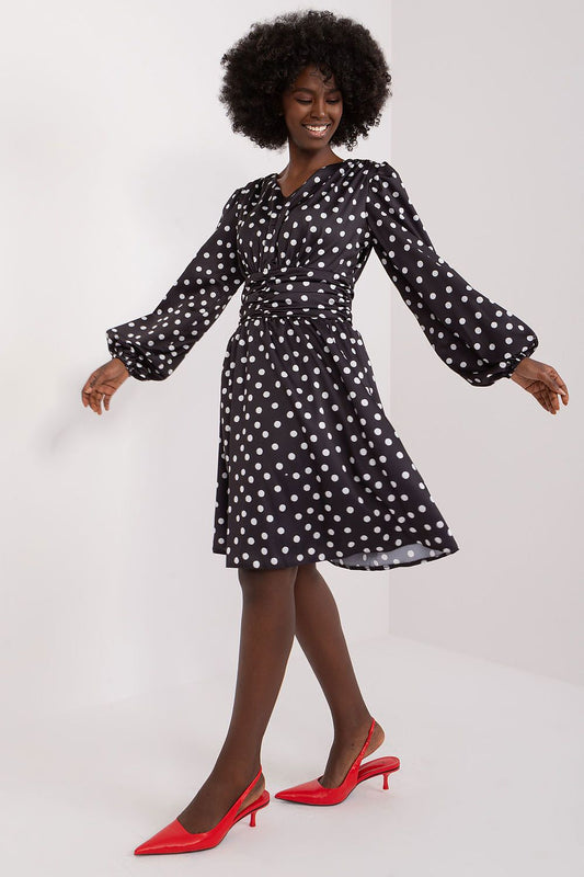 A graceful woman twirling in an exquisitely crafted cocktail dress by Lakerta, characterized by its heart neckline and delicate puff sleeves. The elegant polka dot design complements her movement, while her striking red heels add a touch of sophistication.