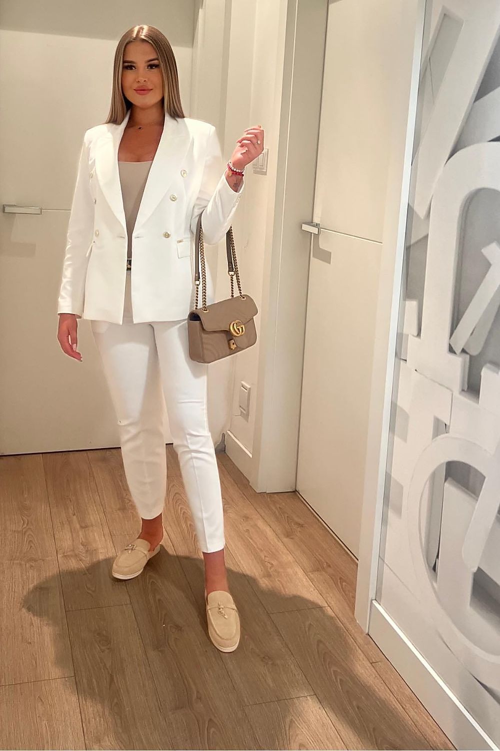 Chic woman wearing an elegant satin lined white blazer jacket by Cabba paired with matching white trousers in a modern interior setting, showcasing a stylish look for any season.