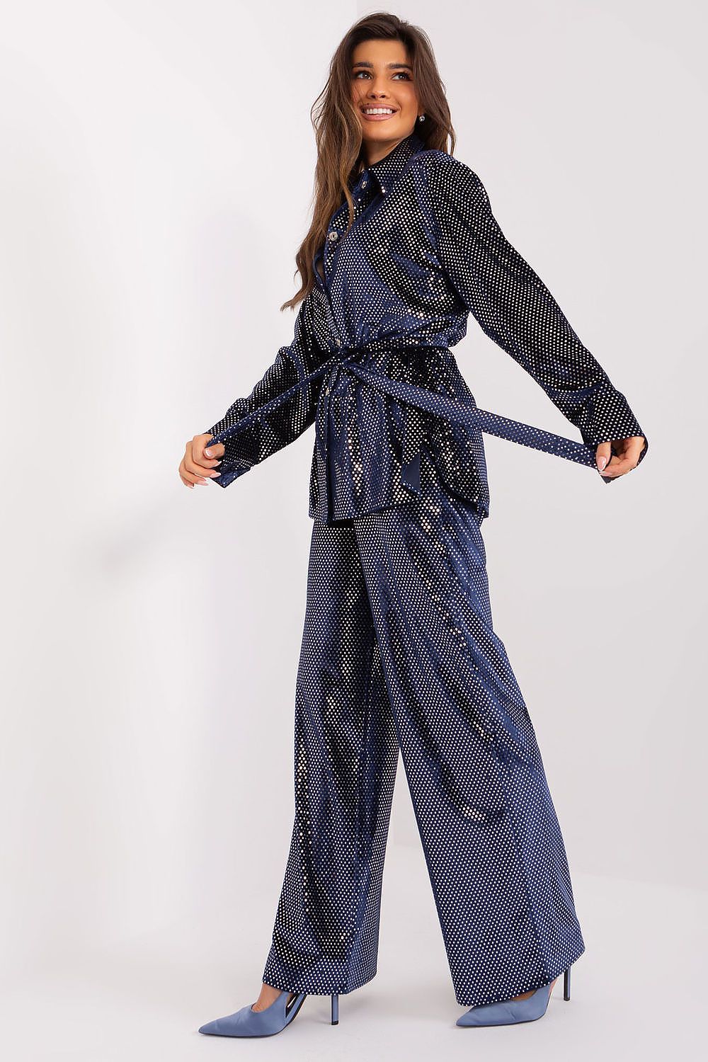 Graceful model wearing a luxurious Lakerta set in navy, with sequin embellishments on the shirt and high-waisted trousers. The playful pose highlights the chic silhouette, perfect for upscale events.