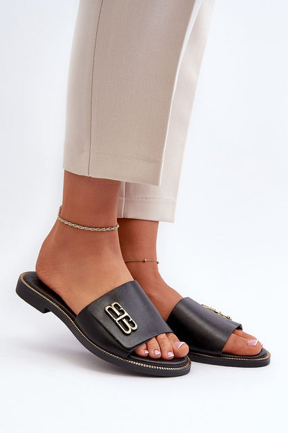 Elegant women's natural leather flip-flops featuring a luxurious gold ornament, styled with chic trousers. Step in style offers exquisite summer footwear.