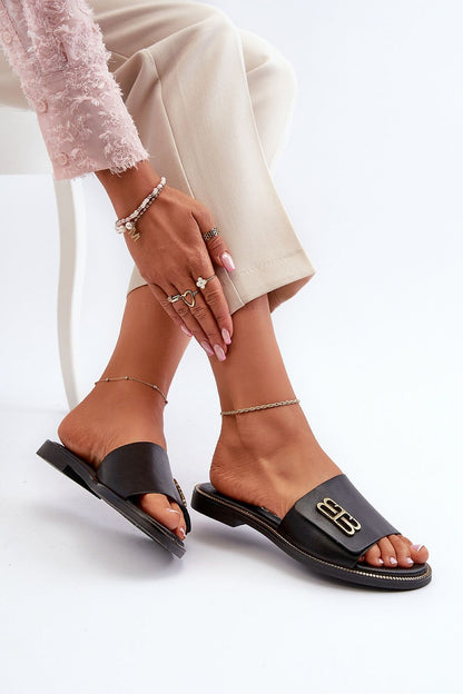 Chic black leather flip-flops adorned with a gold ornament, elegantly paired with stylish trousers. Step in style delivers elegance in summer footwear.