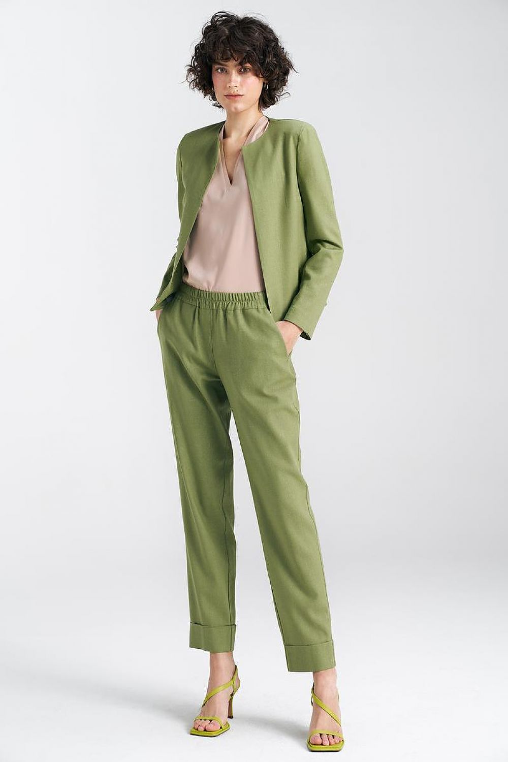Chic model wearing a pistachio green boxy jacket by Nife paired with chic trousers, exuding a modern, stylish aura in a light and fresh atmosphere.