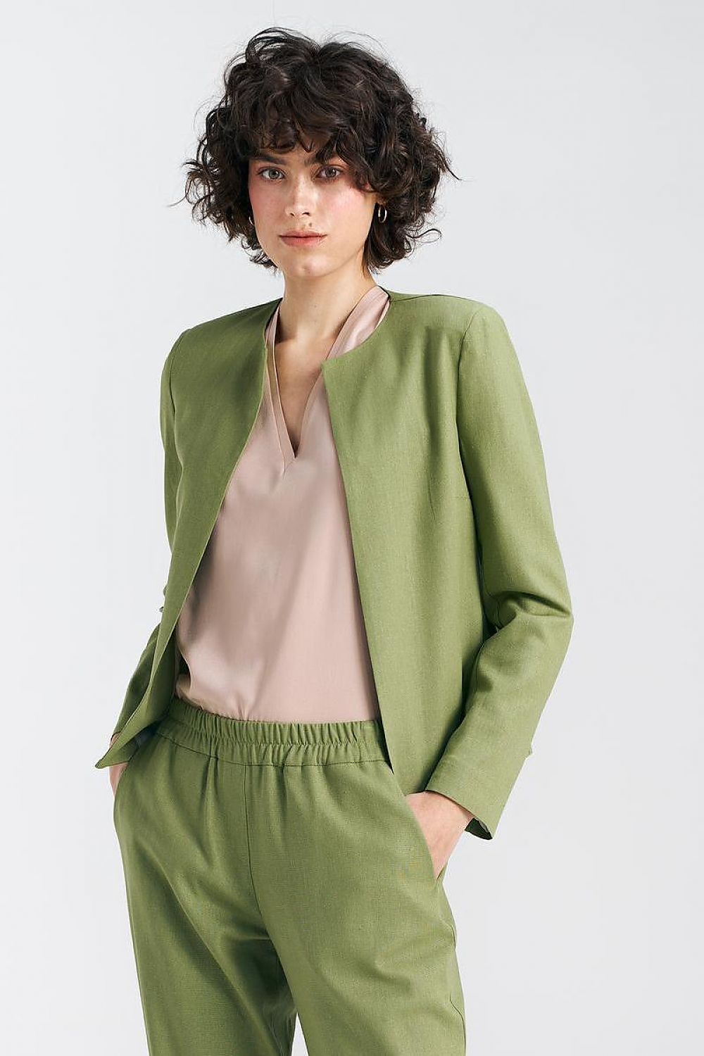 Straight-on view of a model in a pistachio green boxy jacket by Nife, exuding luxury and style with a delicate blouse and sophisticated posture.