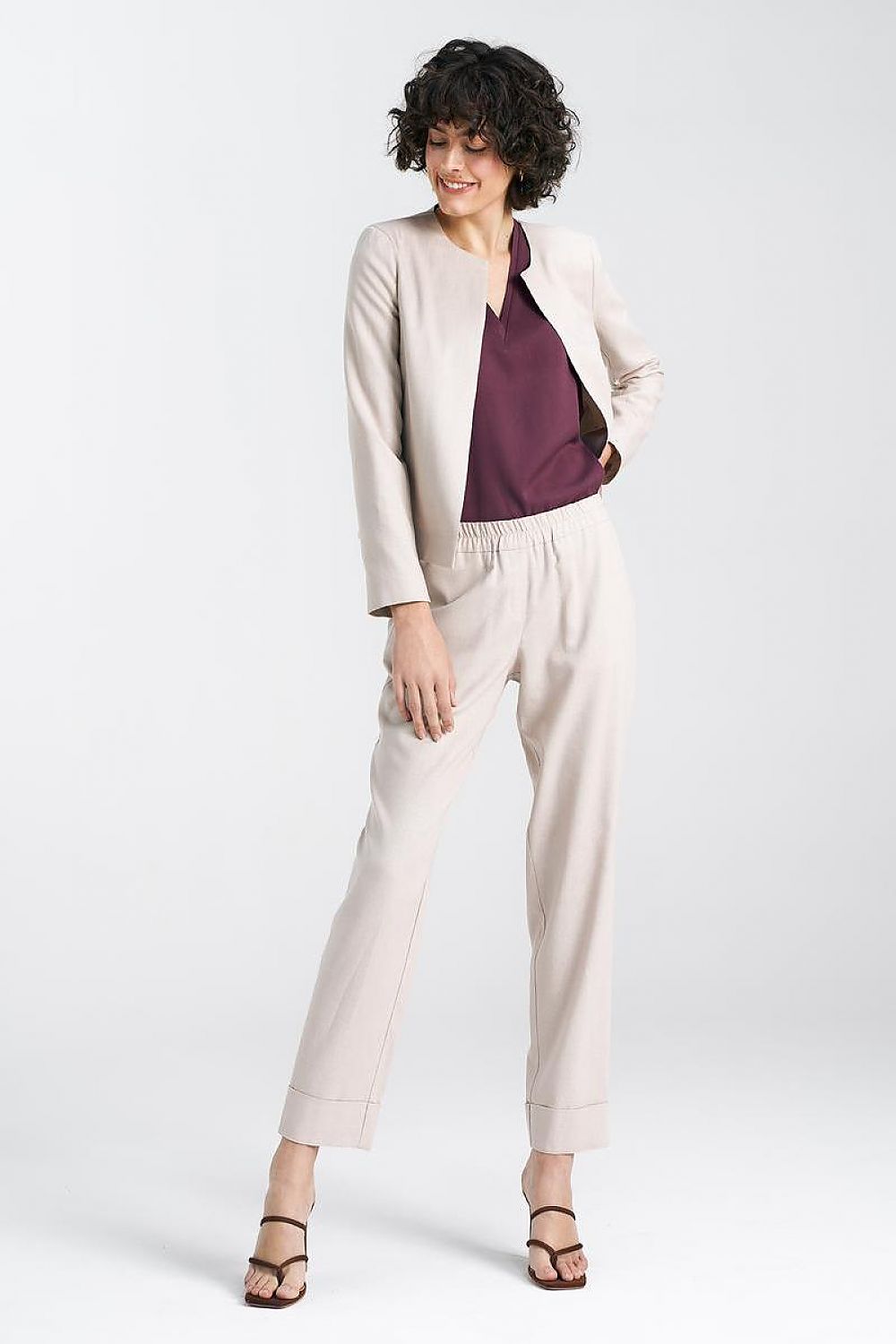 Chic model in a beige jacket with a stylish maroon top and tailored trousers, exemplifying modern elegance from Nife.