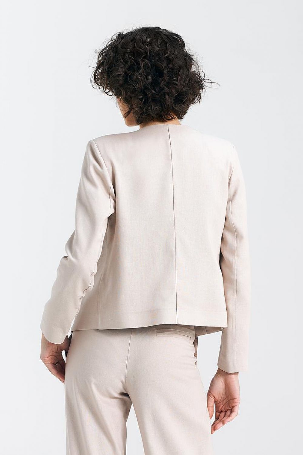 Back view of a fashionable model in a beige jacket, highlighting the structured yet elegant design by Nife.
