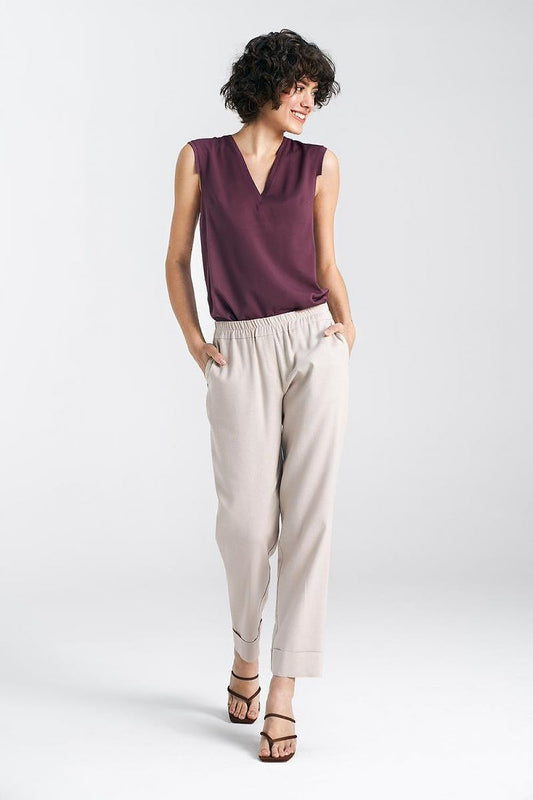 Chic woman modelling a relaxed fit burgundy sleeveless top paired with beige trousers featuring straight legs and cuffs by Nife, embodying effortless elegance and modern style.