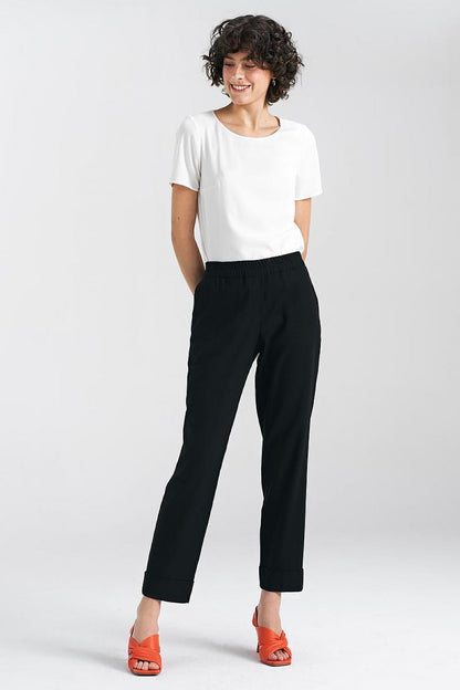 Luxury women's relaxed fit trousers in black by Nife, featuring a straight leg and cuffs, styled with a simple white top and vibrant red sandals, showcasing comfort and elegance.