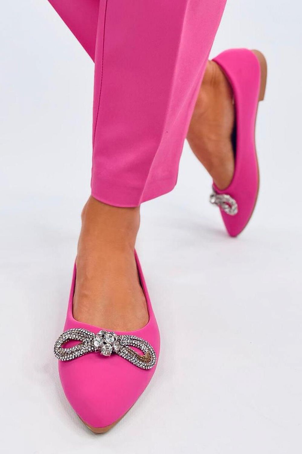 Trendy Inello pink ballerina flats featuring an eye-catching zircon bow, elegantly worn with tailored trousers, exemplifying sophisticated footwear.