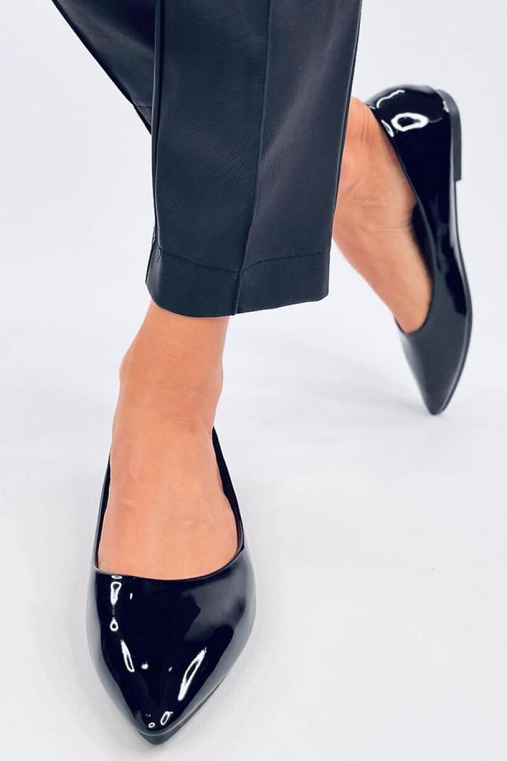 Chic Inello patent leather ballerinas being worn, featuring a graceful cut and modern aesthetic, elegantly paired with tailored trousers for a sophisticated look.