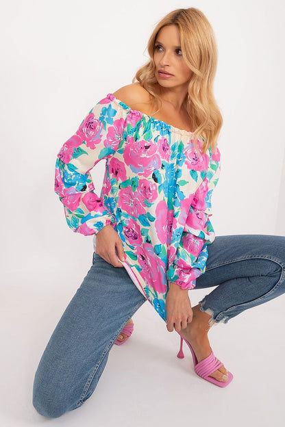 Stylish model wearing a floral print blouse by Rue Paris with off-the-shoulder design, featuring vibrant pink roses against a white background, paired with casual blue jeans and elegant pink heels.