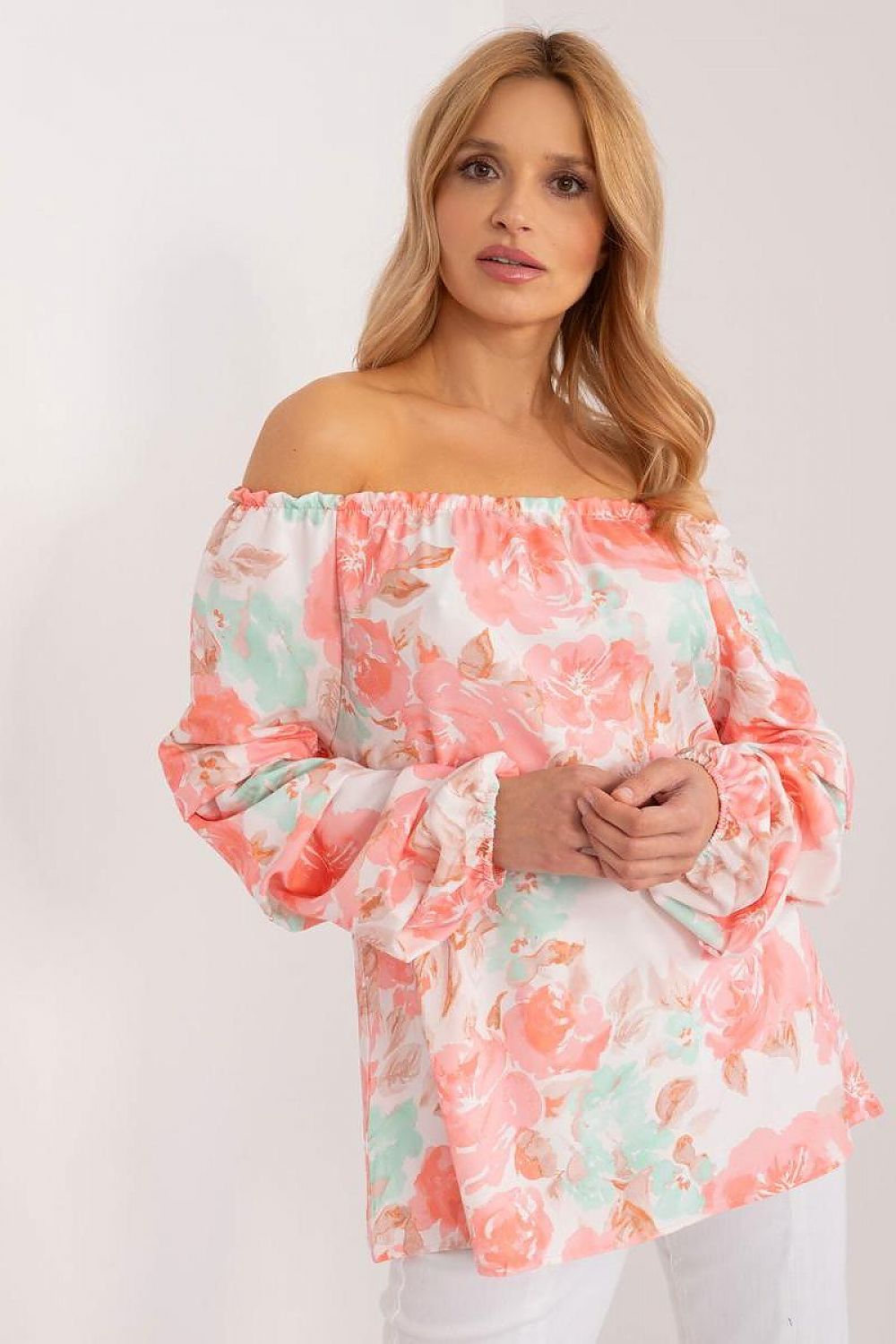 Elegant model showcasing a coral and mint floral print blouse by Rue Paris with a charming off-the-shoulder neckline, complemented by a luxurious setting that enhances its romantic feel.
