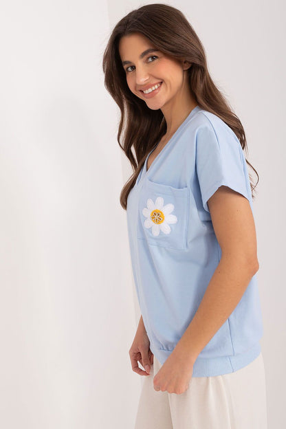 Side view of a model wearing a stylish light blue cotton blouse featuring an embroidered flower and zircon accents by Rue Paris, ideal for chic everyday outings.