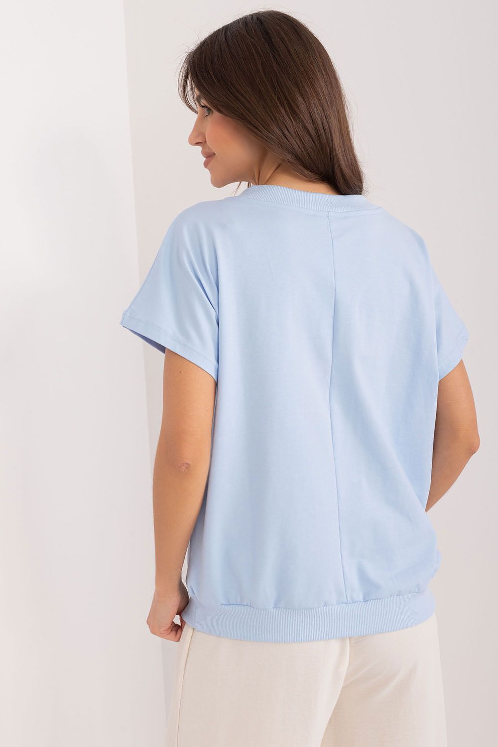 Back view of a graceful model in a light blue cotton blouse with delicate embroidery and zircon embellishments by Rue Paris, highlighting a contemporary casual look.