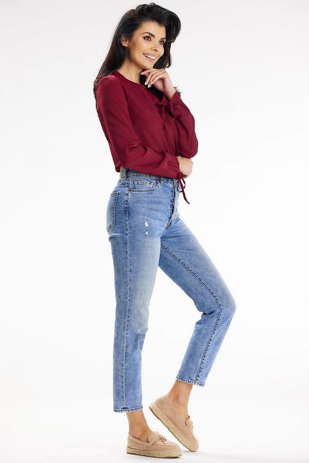 Side profile of a stylish model wearing a trendy burgundy blouse with long sleeves tied at the wrist, complemented by blue jeans, created by Awama.
