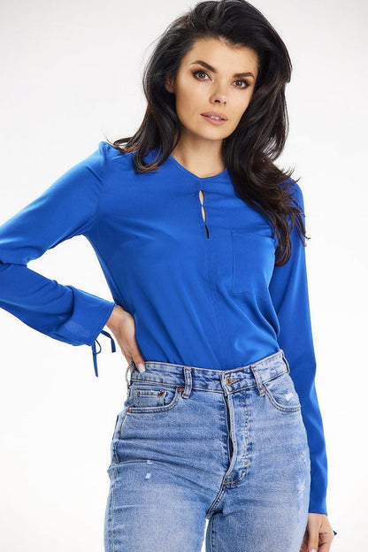 Close-up of a model wearing a sophisticated blue blouse with decorative slits at the neckline, designed by Awama, complemented by high-waisted distressed jeans.