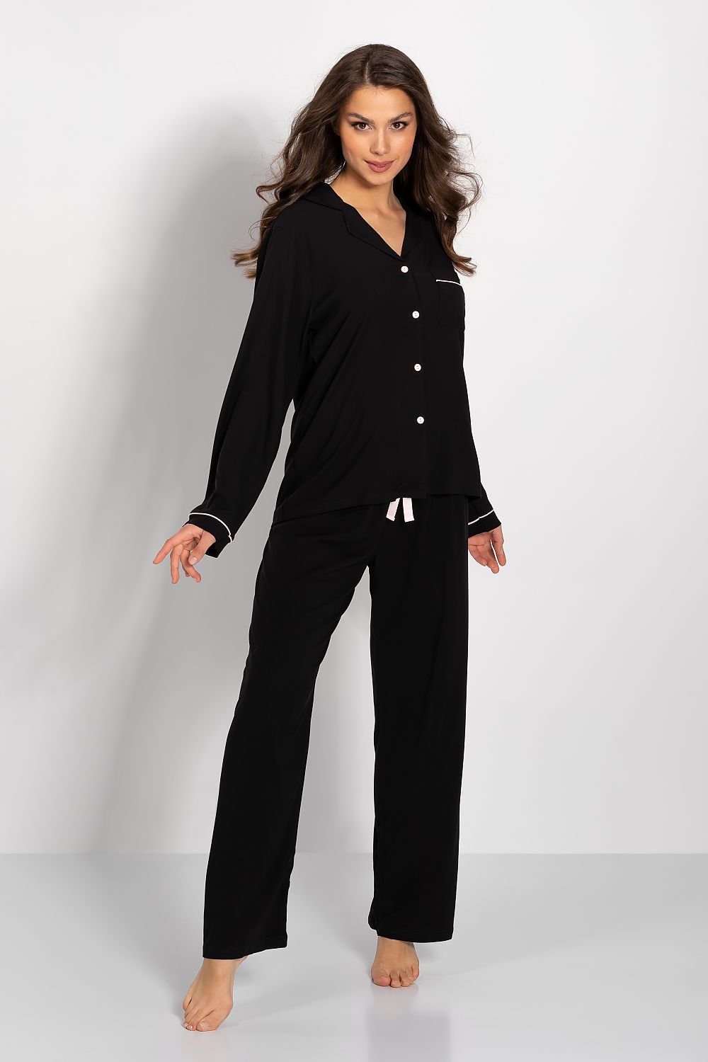 Elegant luxury women's viscose pajamas set in black, featuring long sleeves, piping detail, and satin bow accent, model showcasing a relaxed pose against a minimalistic background.