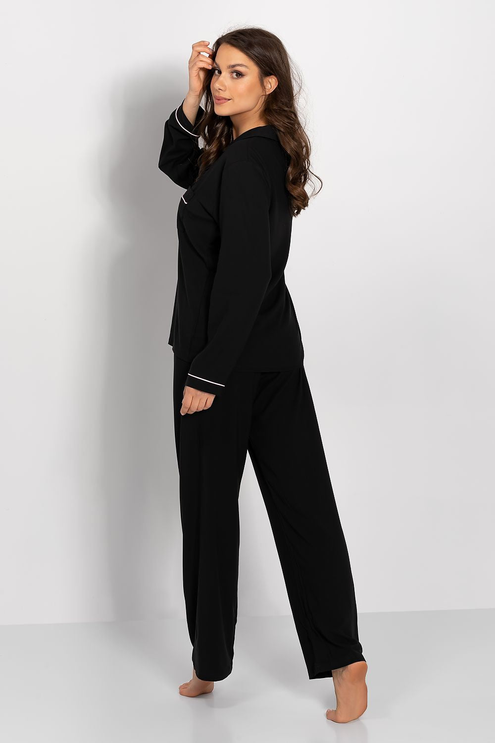 Stylish black women's viscose pajamas with long sleeves and piping, showcasing a side view of the model highlighting the sophisticated satin bow and relaxed fit in a clean aesthetic.
