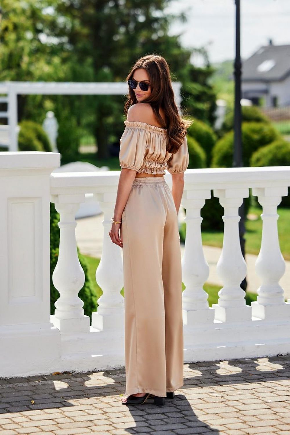 Model wearing the Marbella Satin Blouse by Roco Fashion at a garden party, demonstrating the blouse's suitability for elegant summer events.