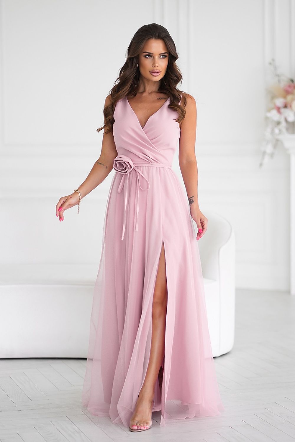 Stunning long dress by Bicotone featuring a sophisticated slit and elegant rose belt, perfect for formal occasions.