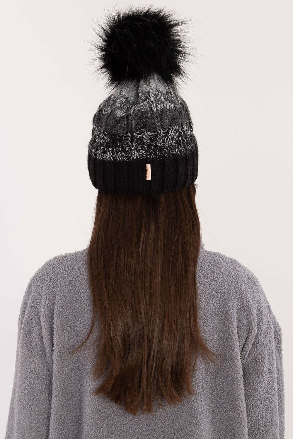 Model wearing a stylish Rue Paris winter beanie, combining elegance and comfort, showcasing its beautiful plaid pattern and fluffy pom-pom.