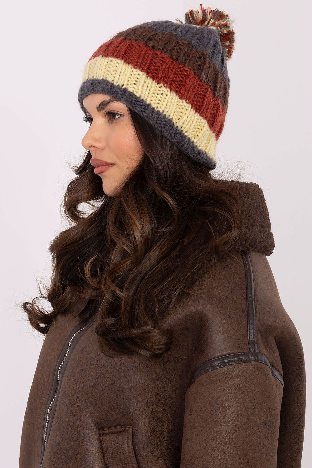 Chic winter beanie from AT showcasing colourful stripes and a plush pom-pom, an essential accessory for cold weather.
