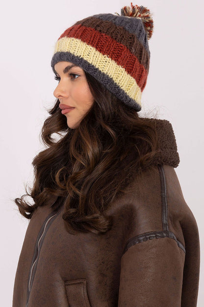 Chic winter beanie from AT showcasing colourful stripes and a plush pom-pom, an essential accessory for cold weather.