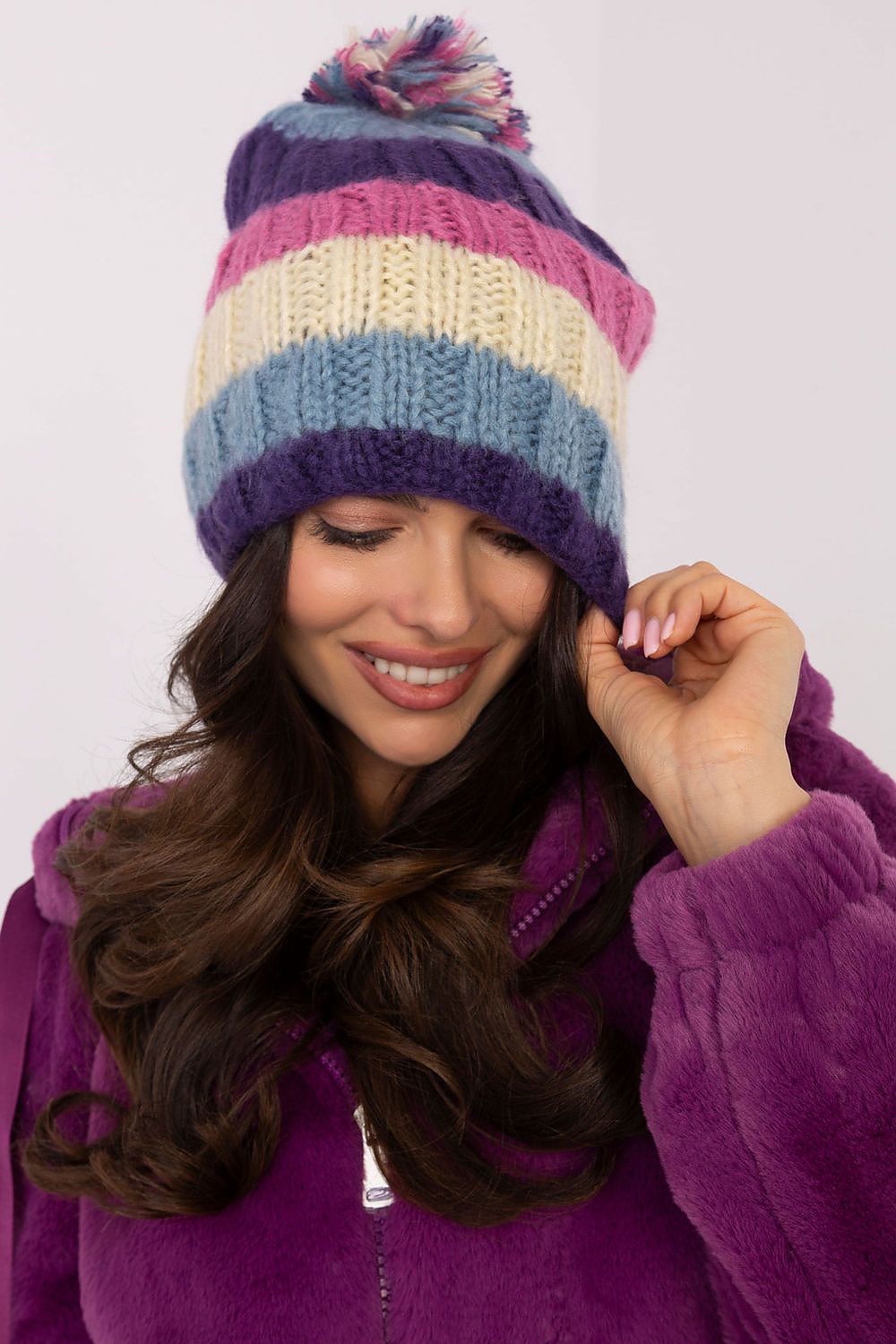 Chic winter beanie hat by AT showcased against a snowy backdrop, highlighting its bright stripes and plush pom-pom.