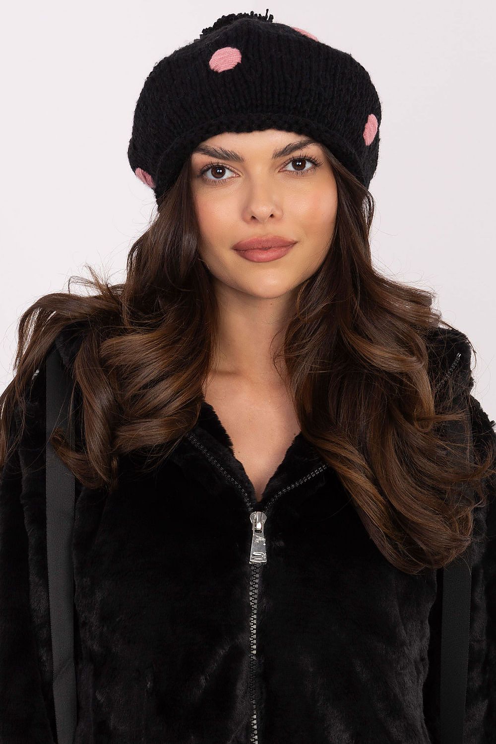 Elegant and fashionable women's winter beanie by AT, featuring a large fluffy pom-pom and decorative dot accents, perfect for adding a touch of luxury to cold-weather outfits.