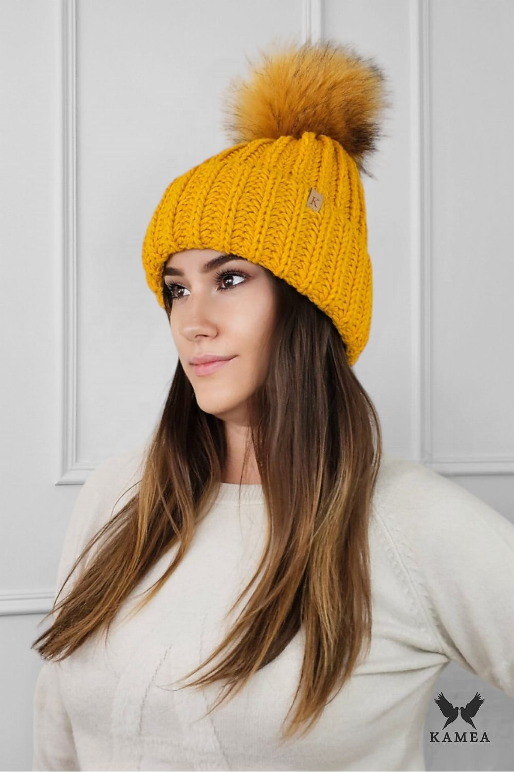 Kamea Nerea Mustard Winter Hat featuring an eco-friendly pompom, expertly crafted from a wool blend for ultimate comfort and style during winter seasons.