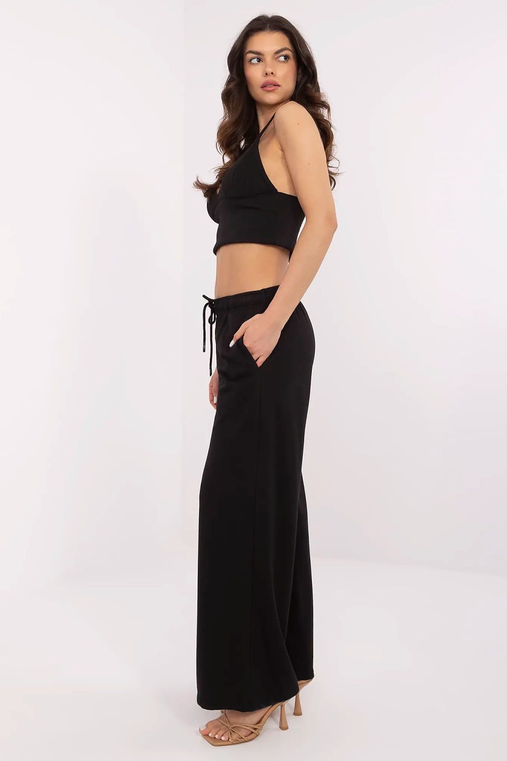 Elegant side view of a model showcasing luxury cotton-blend tracksuit trousers by Relevance, paired with a sleek crop top, in a classic black colour.