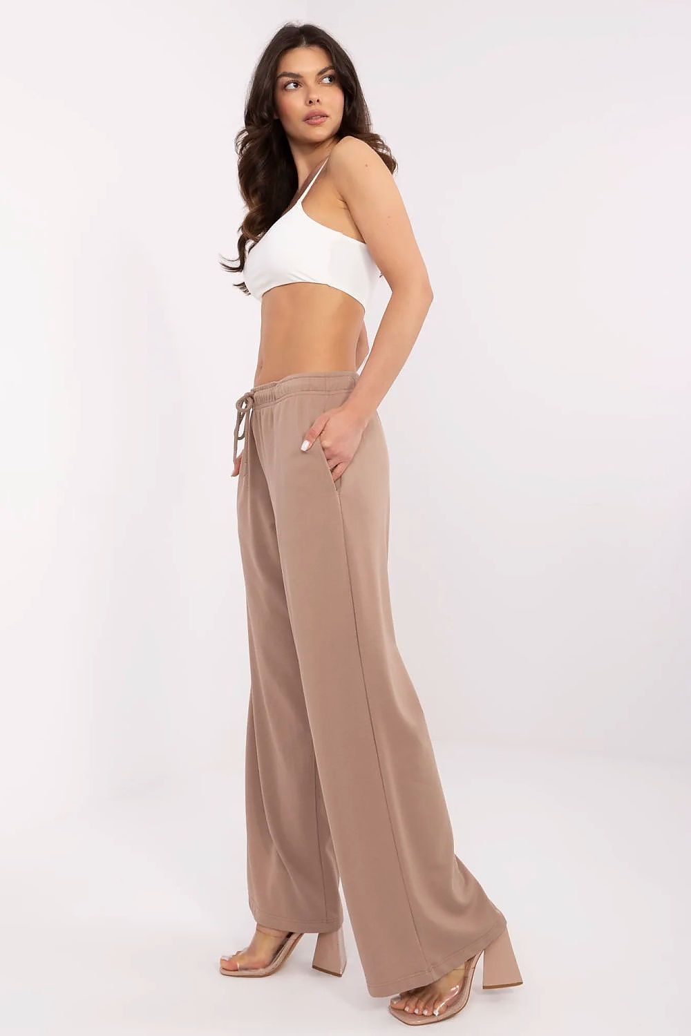 Sophisticated side view of a model in light beige luxury cotton-blend tracksuit trousers by Relevance, highlighted by a fitted white crop top.