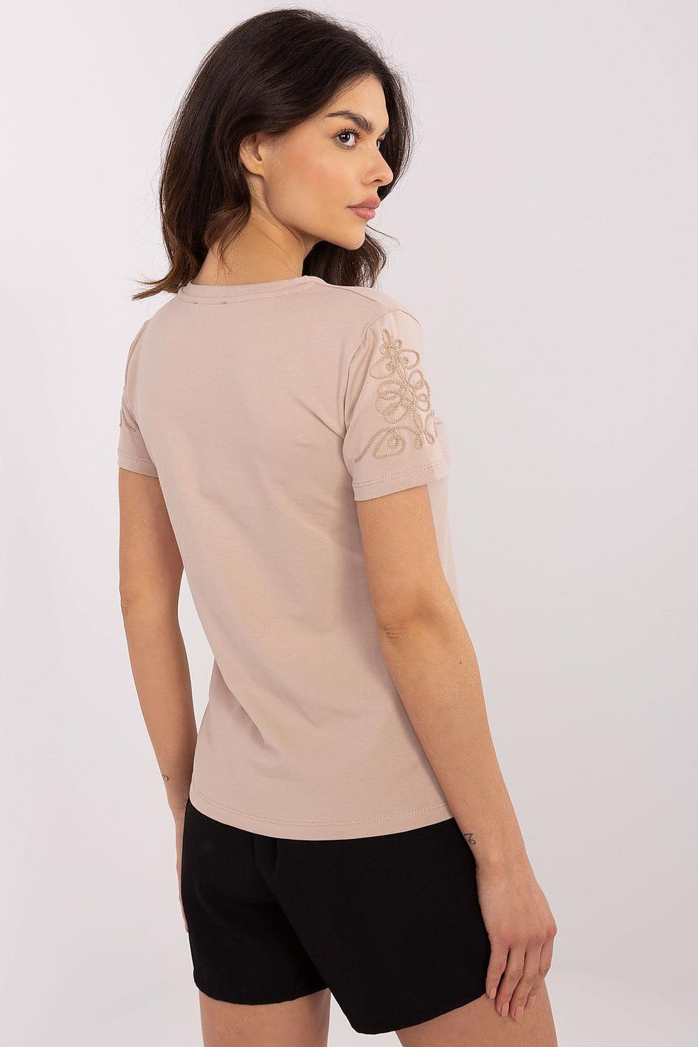Back view of a sophisticated woman in a light beige women's t-shirt by Relevance, highlighting intricate sleeve embroidery, paired with stylish black shorts.