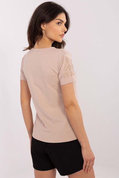Back view of a sophisticated woman in a light beige women's t-shirt by Relevance, highlighting intricate sleeve embroidery, paired with stylish black shorts.