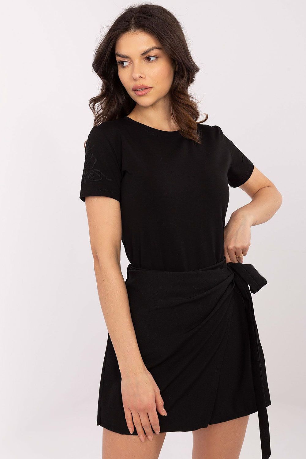 Stylish woman in a luxurious black women's t-shirt by Relevance, designed with subtle embroidery, elegantly paired with a fashionable wrap skirt.