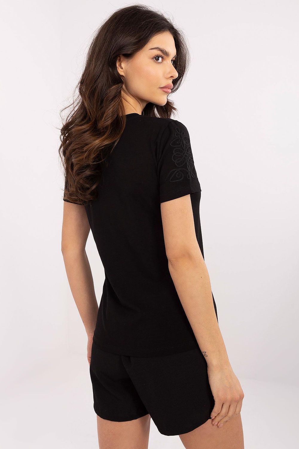 Elegant woman in a black short-sleeved casual t-shirt with unique embroidery, showcasing the stylish design from Relevance. The model is posed from the back, emphasizing the simplicity and sophistication of this soft cotton blend top.