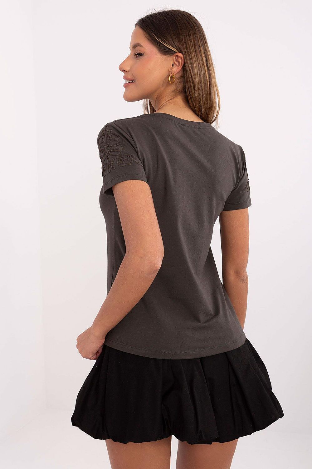 Stylish woman displaying the back of a grey t-shirt with intricate embroidery from Relevance. The model is outfitted with a black skirt, effortlessly blending casual charm with luxurious comfort.