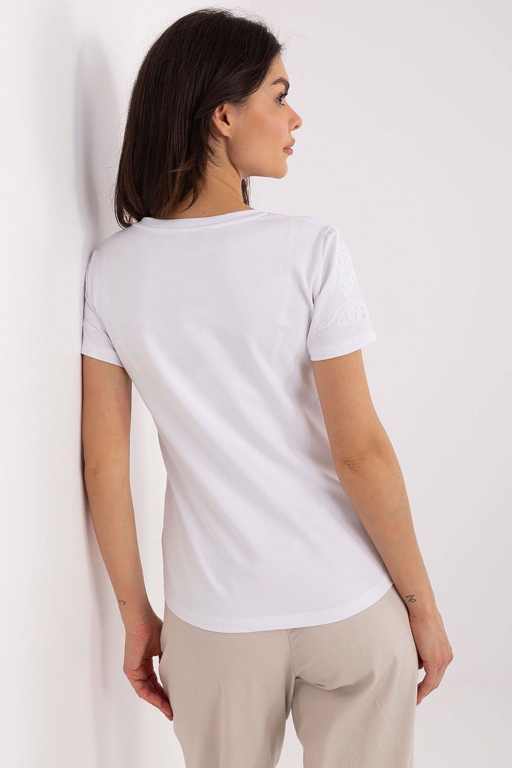 Sophisticated back view of a women's casual t-shirt by Relevance, highlighting the subtle embroidery on short sleeves, paired with chic trousers in a light, airy environment.
