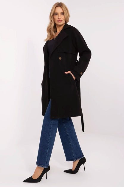 Elegant women's knee-length double-breasted coat in black by Och Bella, featuring a waist tie, styled with denim and heels.