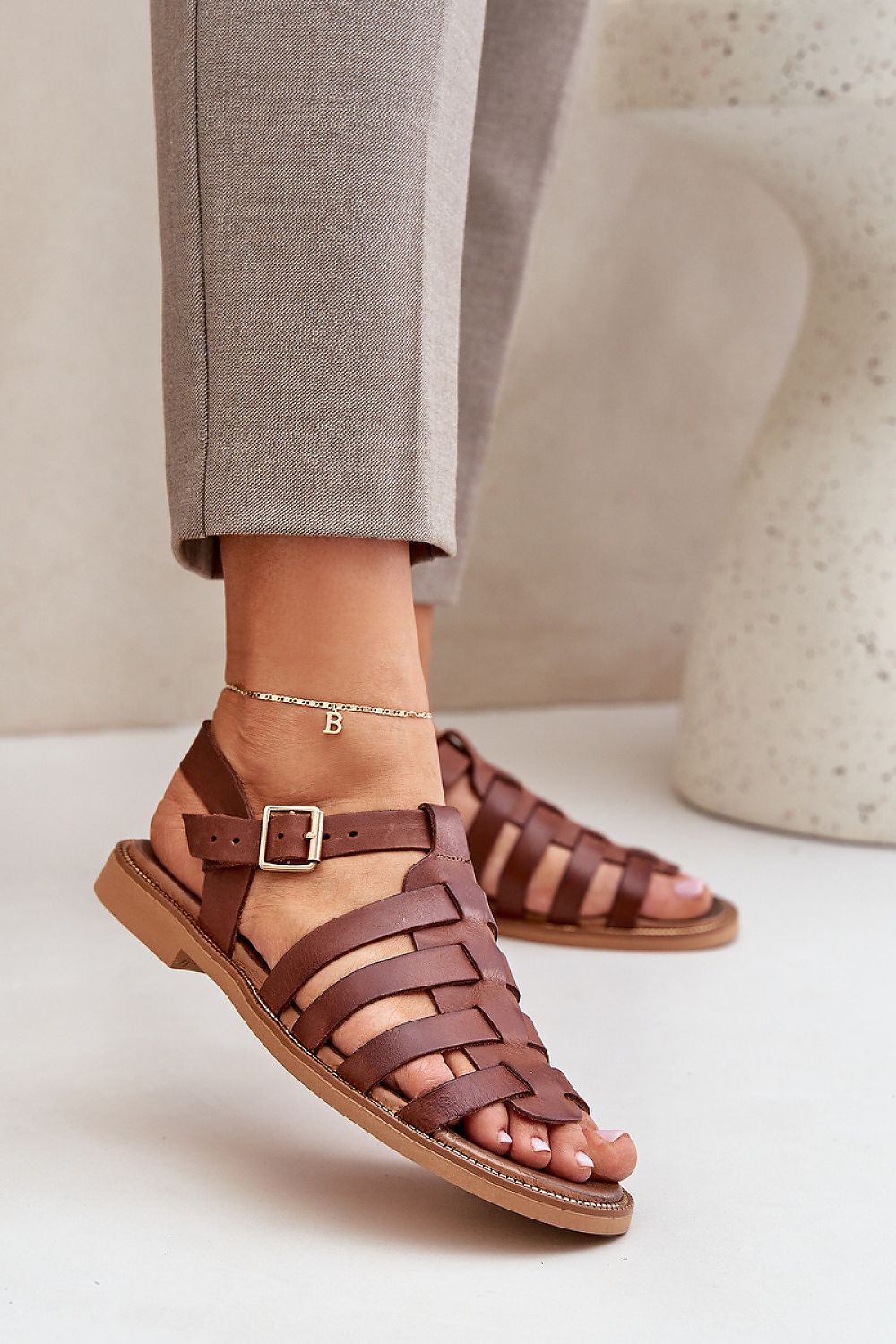 Stylish brown natural leather sandals by Step in Style, highlighted with an adjustable strap and a sleek woven pattern, presented elegantly on a model's foot.