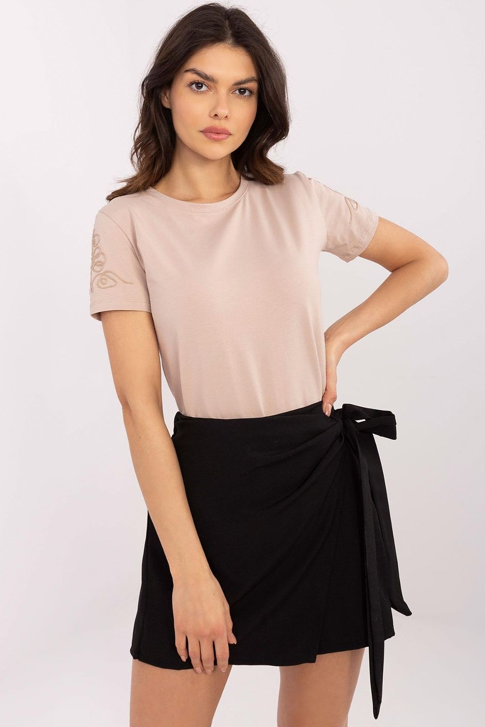 Confident woman in a light beige women's t-shirt by Relevance, featuring delicate embroidery, complementing a chic wrap skirt for a luxurious casual look.