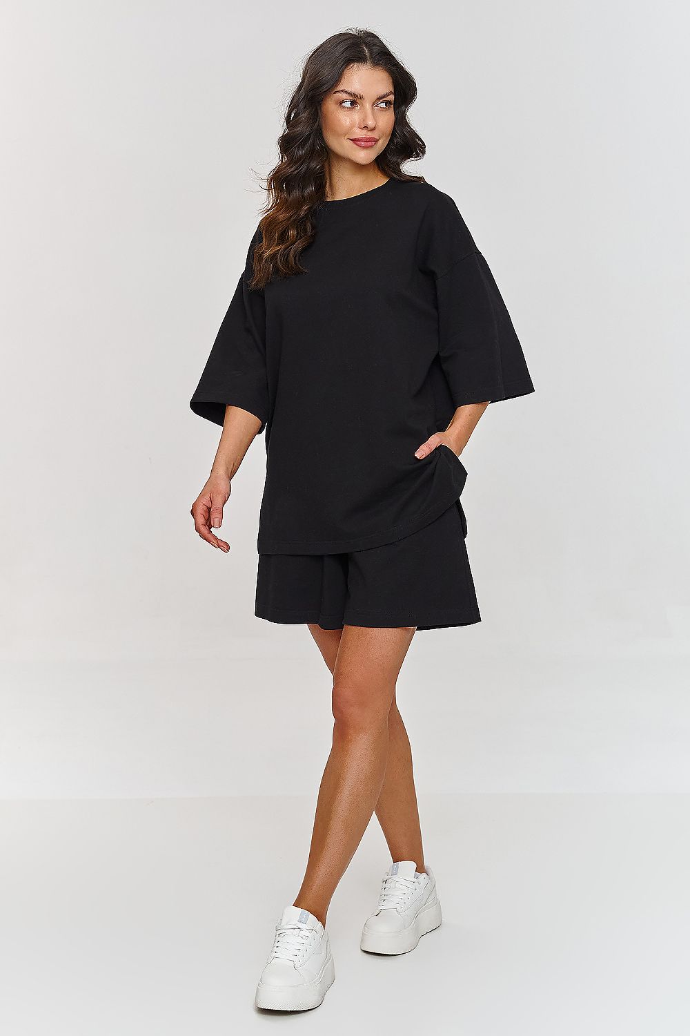 Chic woman presenting a fashionable black tracksuit set by Makadamia, featuring a loose fit t-shirt and shorts, ideal for casual outings.