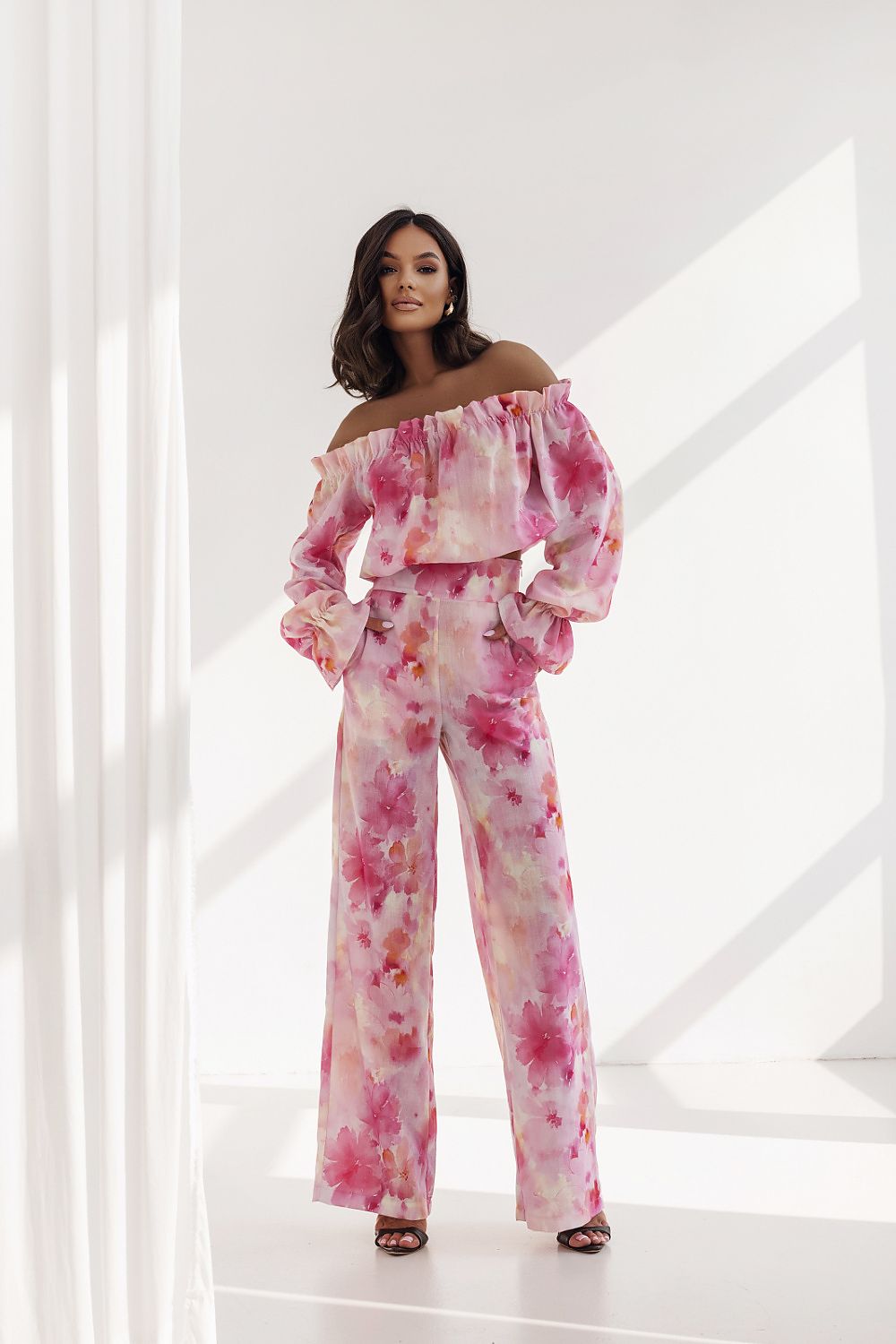 Luxurious women's outfit by LaBalancia, displaying a romantic off-the-shoulder frilled blouse paired with high-waisted trousers in a delicate pink floral design, ideal for elegant events.