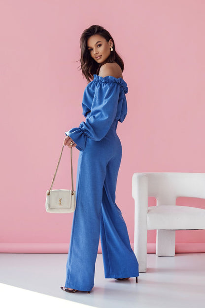 Chic view of an elegant blue women's outfit with a frilled off-shoulder blouse and high-waisted trousers, complemented by a stylish handbag, designed by LaBalancia.