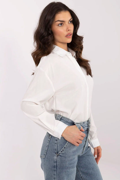 Side view of a sophisticated women's white shirt by NM, showcasing long sleeves and a polished collar, elegantly complemented by denim trousers for a chic outfit.