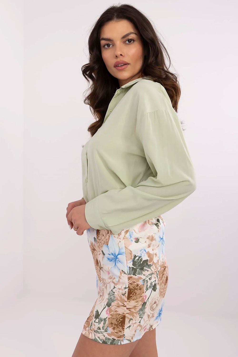 Side view of NM's elegant long sleeve women's shirt in green, showcasing its fitted silhouette and classic collar, complemented by a chic floral skirt.